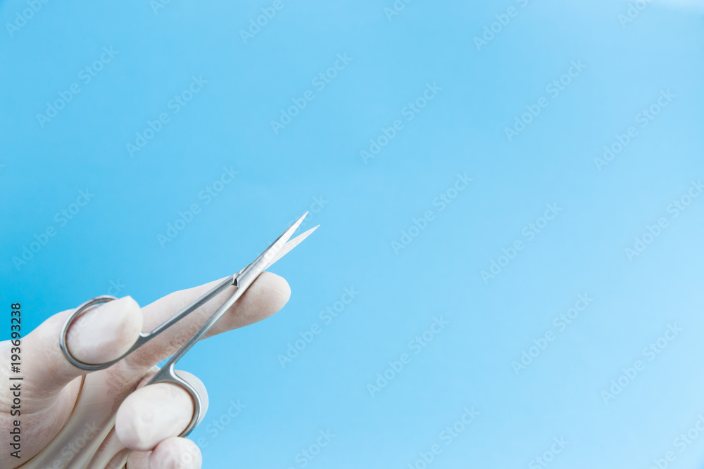 Scissors in doctors hands in white medical gloves isolated on blue background copy space Scissors in doctors hands in white medical gloves isolated on blue background copy space