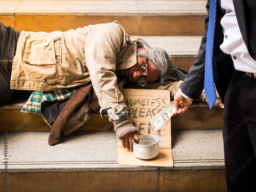 A businessman gives money to a homeless man sleeping on a ladder