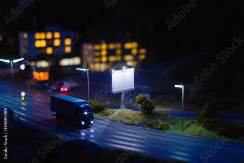 Model or layout of a Billboard on an asphalt road at night. The concept of a Billboard. Blank advertising billboard in the city at night. tilt shift effect.
