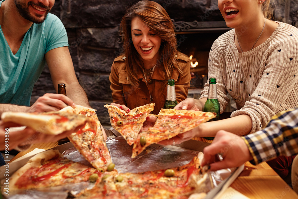 laughing friends eating pizza and having fun. They are enjoying eating and  drinking together Stock Photo