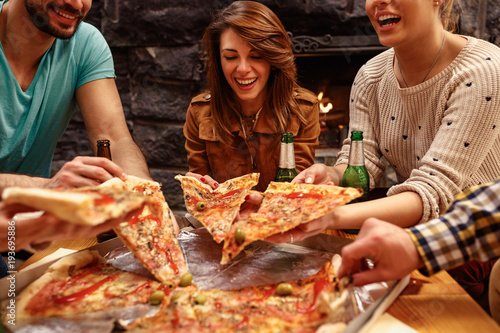 laughing friends eating pizza and having fun. They are enjoying eating and drinking together