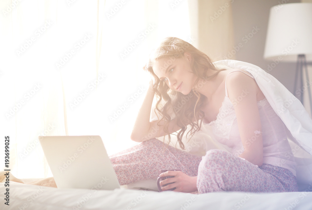 Young beautiful woman sitting in bed with laptop. Young beautiful woman sitting in bed with laptop.