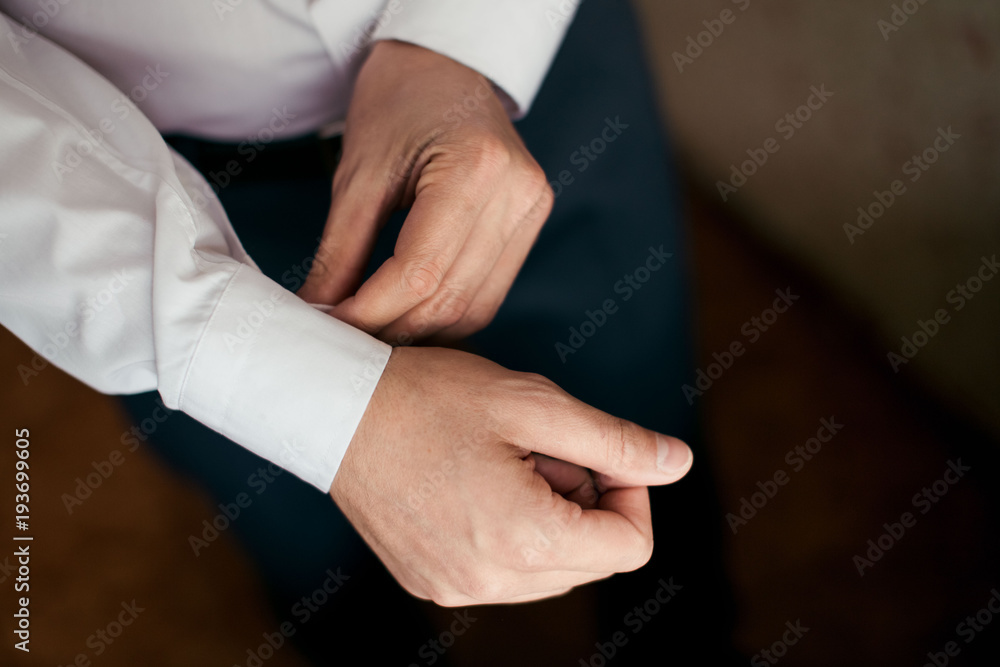 Groom in a white shirt fastens the cuff on his arm
