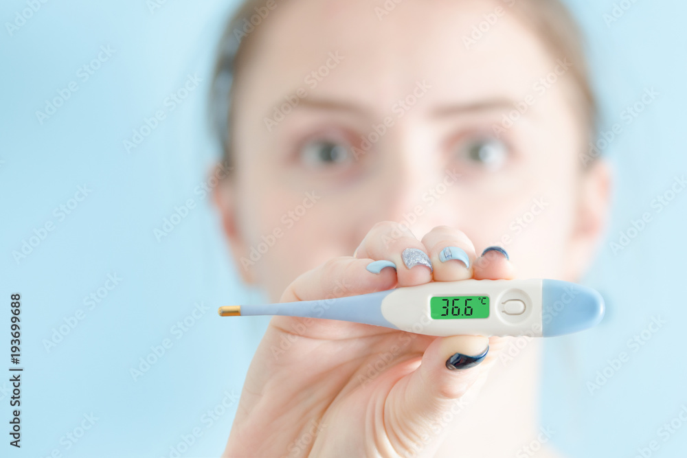 Woman with a thermometer in his hand. Normal body temperature. Face on background Woman with a thermometer in his hand. Normal body temperature. Face on background