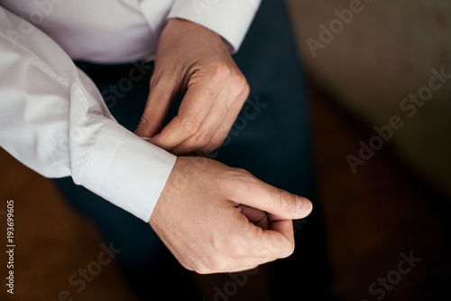 Groom in a white shirt fastens the cuff on his arm