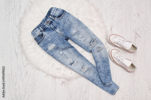 Blue ragged  jeans and white sneakers on white fur. Fashionable concept