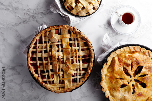 Pie crust design ideas - various ways of pie decoration with lattice and leaves. Apple, strawberry and raspberry pies cooked and served with tea on white marble table