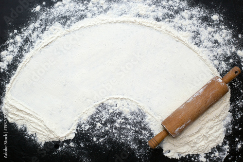 View from above. Flour and a wooden rolling pin on a dark background. For circular text