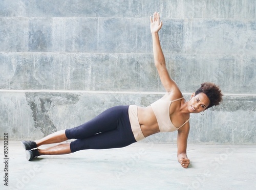 Melanesian pacific islander athlete girl with afro performing exercising routines plank with twist, one hand raised © Hagen Production