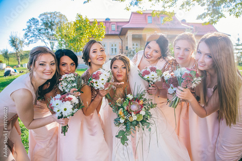 Outdoor portrait of beautiful young bride with her female friends. Funny bridesmaids with bewlyweds at sunny park.