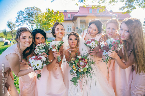 Outdoor portrait of beautiful young bride with her female friends. Funny bridesmaids with bewlyweds at sunny park.