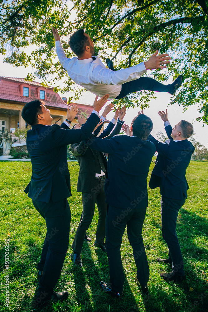 Wedding funny day. Groomsmen throw groom up standing in the park.