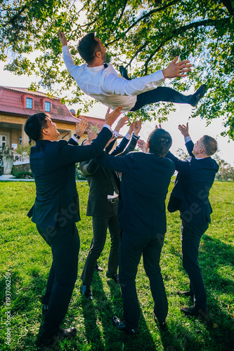 Obraz na płótnie Wedding funny day. Groomsmen throw groom up standing in the park. w salonie
