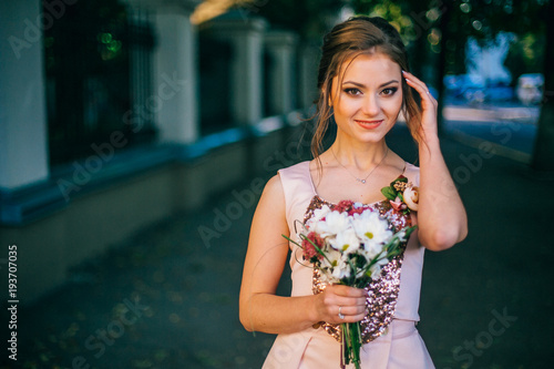 Portrait of a beautiful bridesmaid posing with bride's wedding bouquet in city streets with green trrees. Amaizing wedding day. photo