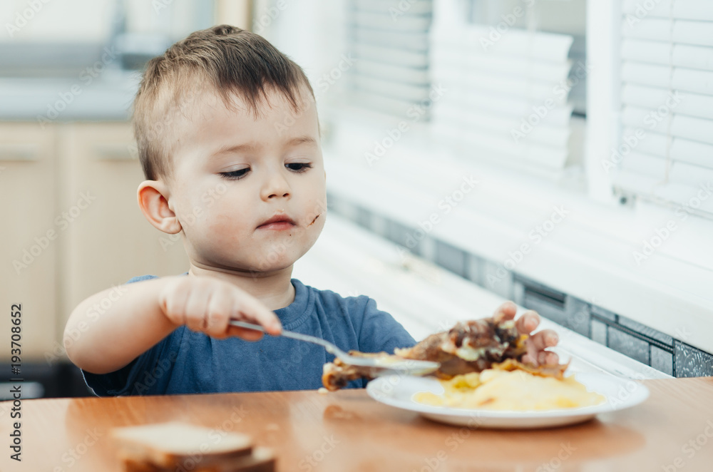 child in the kitchen eating mashed potatoes, spoon, next to the plate is a piece of chicken meat child in the kitchen eating mashed potatoes, spoon, next to the plate is a piece of chicken meat