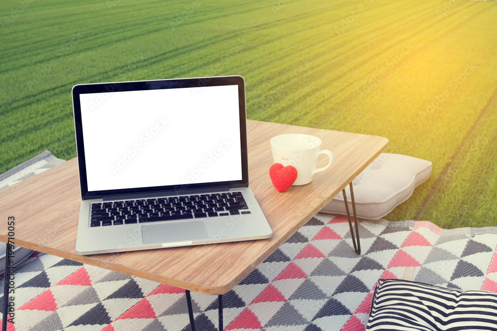 picnic table with blank screen on laptop and white coffee cup, red heart shape at green lawn garden. concept of workplace in holiday. picnic table with blank screen on laptop and white coffee cup, red heart shape at green lawn garden. concept of workplace in holiday.