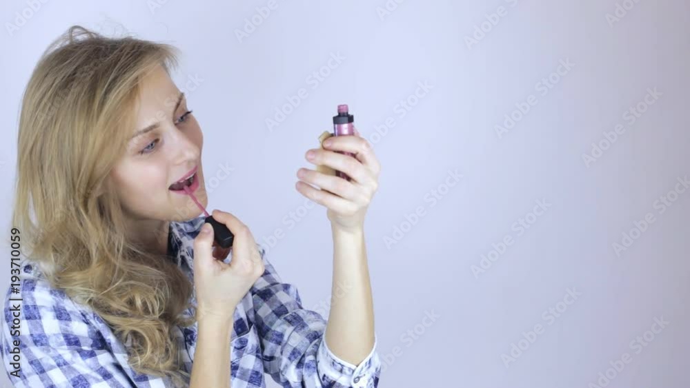 Beautiful woman paints her lips looking on little mirror Beautiful woman paints her lips looking on little mirror