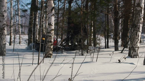 Man maneuvering on mini snowmobile on deep snowdrifts in the forest between the trees photo