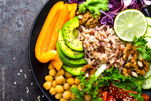 Fototapeta Naklejka Na Ścianę i Meble -  Buddha bowl dish with brown rice, avocado, pepper, tomato, cucumber, red cabbage, chickpea, fresh lettuce salad and walnuts. Healthy vegetarian eating, super food. Top view