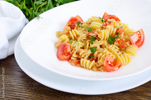 Warm salad with seafood in a white bowl on a wooden background. Pasta Radiatori with crayfish, shrimp, tomatoes, herbs and creamy garlic sauce.