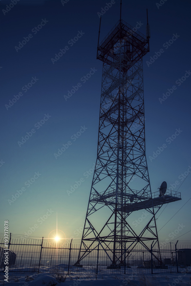a metal tower at dawn behind a barbed wire.