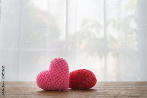 Wood Office table with Beautiful  Couple knitted fabric heart shape  on white curtain windows texture background. view from front office table. concept of valentine's day and heath care.