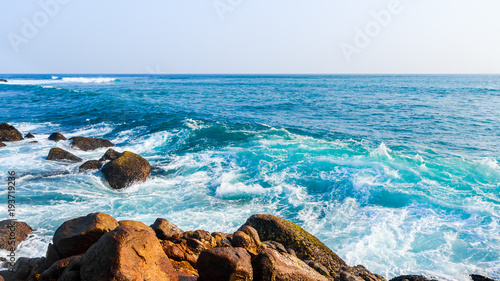 Beautiful turquoise wave crashing on rocks in tropical ocean with big splash. Close up.