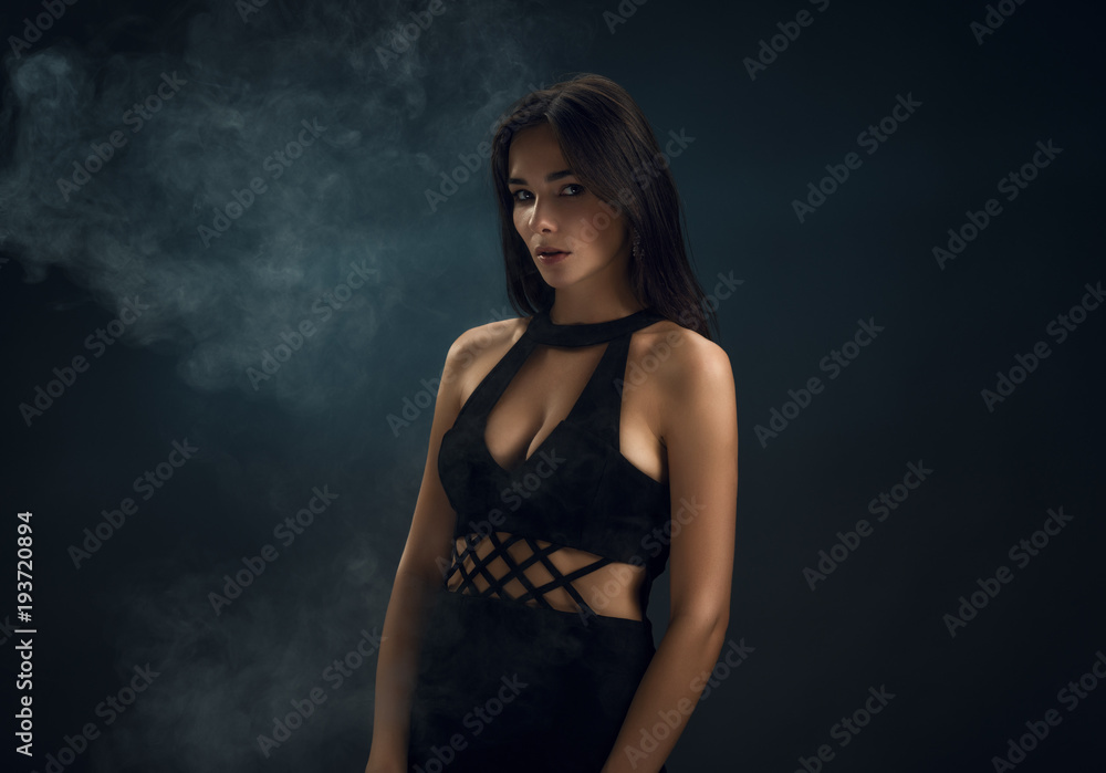 Beautiful girl in a black dress in the smoke. Dark background. Beautiful girl in a black dress in the smoke. Dark background.