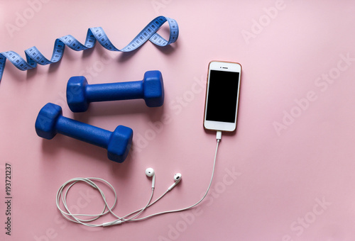 on a pink background dumbbells blue color ribbon centimeter phone smartphone with headphones white 