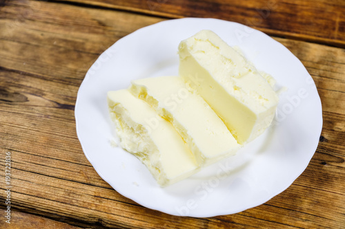 Fresh farm piece of butter on a white plate on wooden background. Farm products.