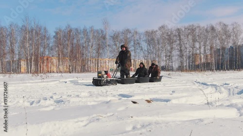 Three men in winter clothes overcoming the deep snow on a mini snowmobile with a trailer photo