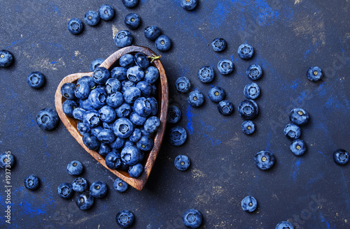 Fresh blueberries in a wooden bowl in the shape of a heart on a dark background, top view