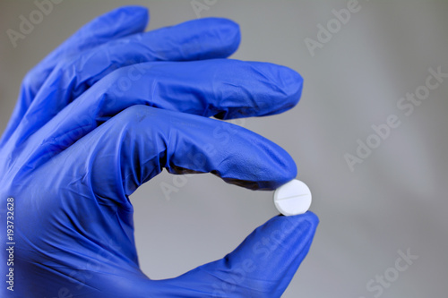 A hand in a blue medical glove holds a tablet close up, selective focus, blurred neutral background
