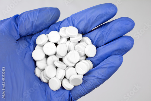 white pills in hand blue medical glove close up, selective focus, blurred neutral background