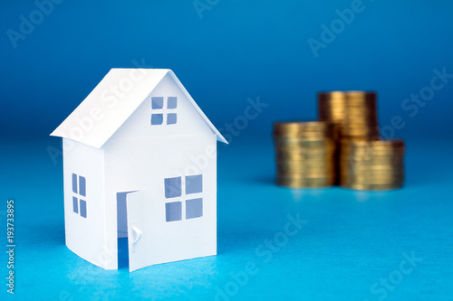 white small house and golden coins on blue background, Real Estate concept close up, selective focus