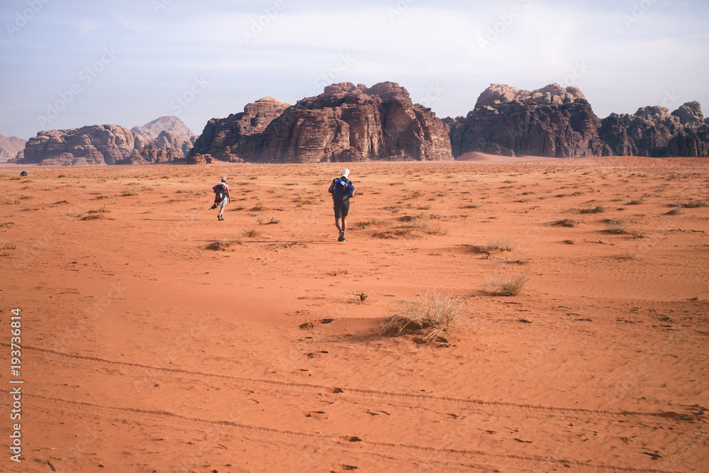 Two hikers in a sand desert. Tourist friends in Jordan natural park Wadi Rum.Group of backpackers walking on the road. Natural background.