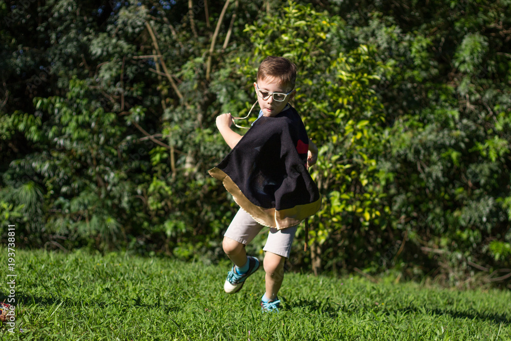 blond boy wearing black cape playing running jumping having fun in a natural green garden real scene blond boy wearing black cape playing running jumping having fun in a natural green garden real scene