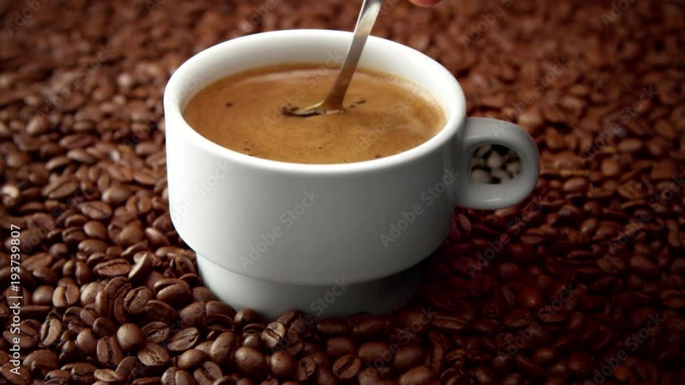 side view of white cup of black coffe on coffee beans. spoon mooving coffe side view of white cup of black coffe on coffee beans. spoon mooving coffe