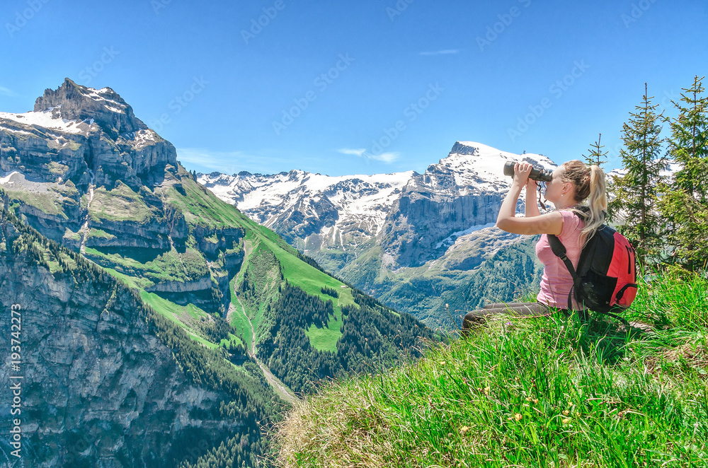 girl traveler looks through binoculars, against a backdrop of mountain peaks, admires the nature and mountain landscapes of Switzerland, the Engelberg resort