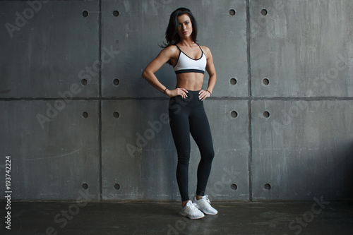 young adult girl stand near concrete wall in gym in sportswear