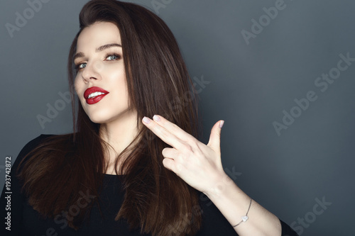 Foto Portrait of beautiful smiling woman with perfect make up holding her fingers in the shape of the gun pretending to shoot herself