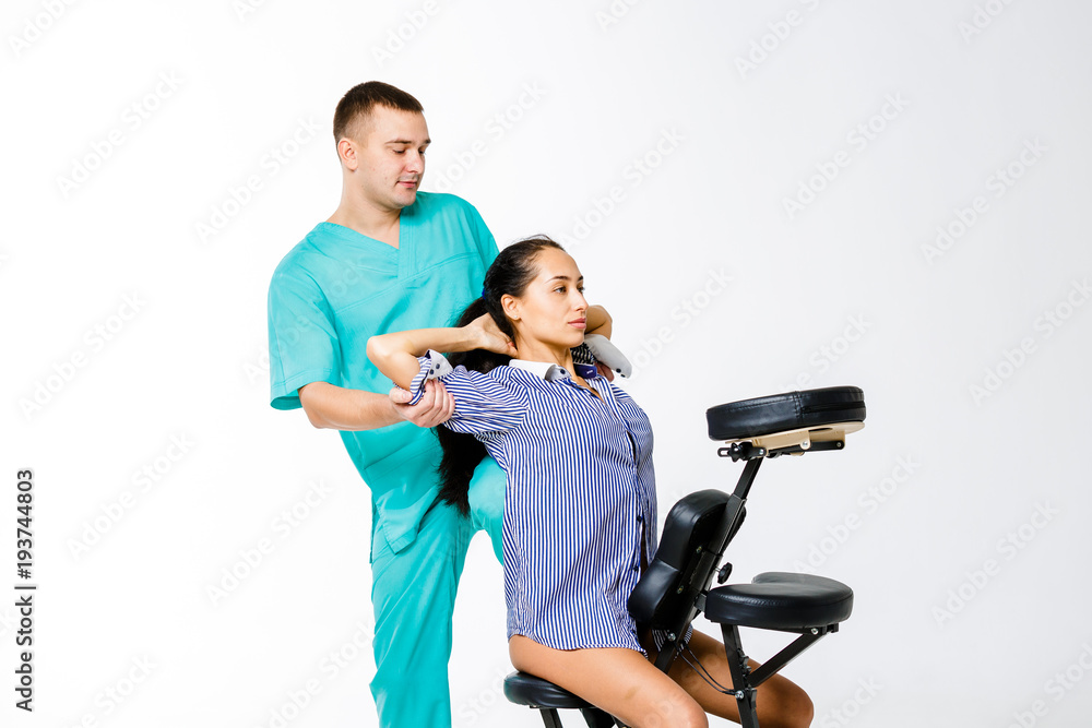 Theme massage and office. young male therapist in blue suit doing back massage with his knee braced in the spine of female worker, business woman in shirt on shiatsu massage chair for fatigue relief Theme massage and office. young male therapist in blue suit doing back massage with his knee braced in the spine of female worker, business woman in shirt on shiatsu massage chair for fatigue relief
