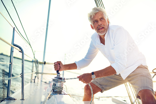 Photos Mature man winching sail ropes on his boat