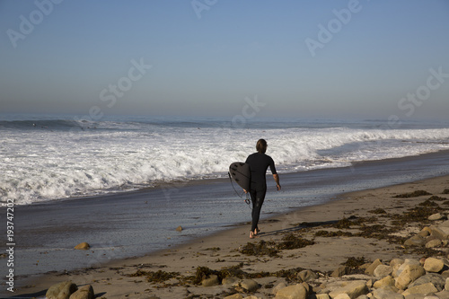 A man carries a surfboard as he walks along the beach © FluidFrame