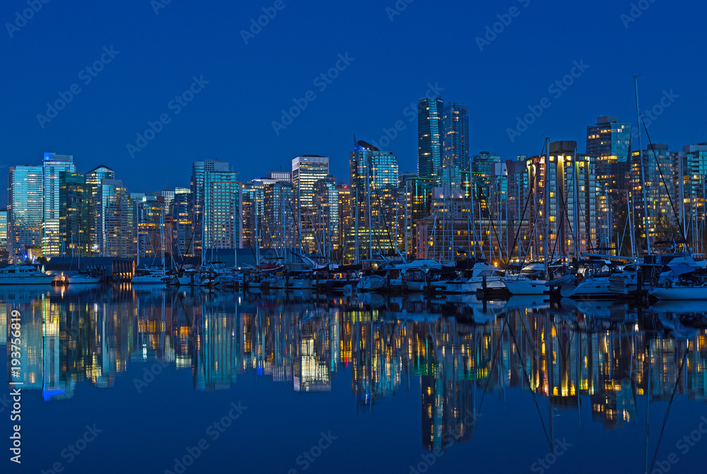 Vancouver city skyline at night in British Columbia, Canada. Modern building and waterfront marina with reflection in calm waters.
