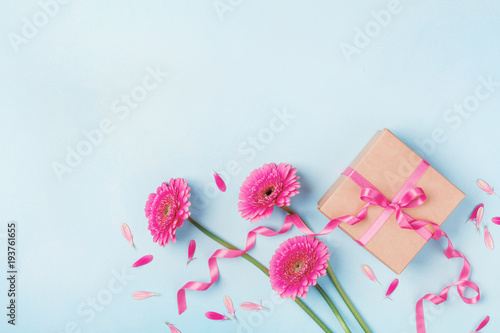 Spring card for Birthday, Woman or Mothers Day. Pink flowers and gift box on blue table top view. Flat lay.