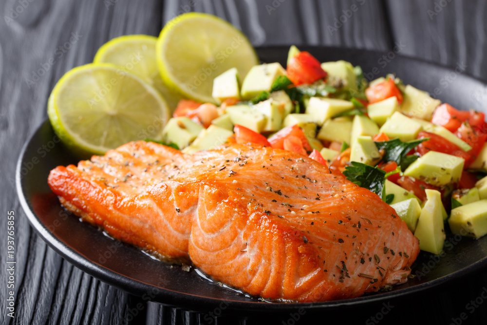 Freshly cooked salmon steak with lime, avocado and tomatoes close-up on a plate. horizontal Freshly cooked salmon steak with lime, avocado and tomatoes close-up on a plate. horizontal