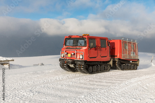 Red ratrak snowcat in winter mountains. A red snow tucker covered with snow.