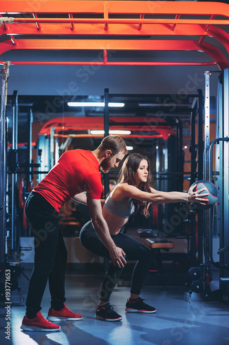Personal trainer helps the girl to do exercises in the gym