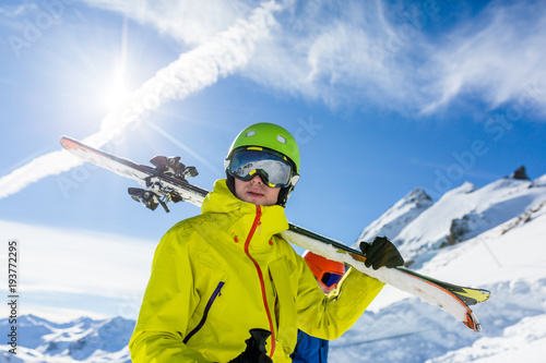 Photo of sports man wearing helmet and mask, with skis on his shoulder